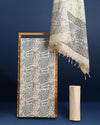 Off white and slate blue Katan silk unstitched suit set hand block printed with stylised swirls and fish motifs in an asymmetric repeat, with teal and charcoal grey accents and fringed edges.