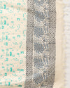 Off white and slate blue Katan silk unstitched suit set hand block printed with stylised swirls and fish motifs in an asymmetric repeat, with teal and charcoal grey accents and fringed edges.