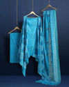 Sky blue Katan silk unstitched suit set block printed with tribal figures and circular mandalas in bright and light blue on the top piece, a dupatta bordered with linear geometric bands, and a plain bottom piece.