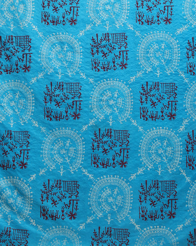 Sky blue Katan silk unstitched suit set block printed with tribal figures and circular mandalas in bright and light blue on the top piece, a dupatta bordered with linear geometric bands, and a plain bottom piece.