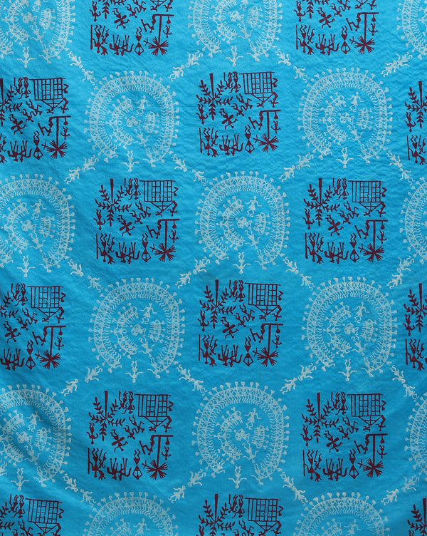 Sky blue Katan silk unstitched suit set block printed with tribal figures and circular mandalas in bright and light blue on the top piece, a dupatta bordered with linear geometric bands, and a plain bottom piece.