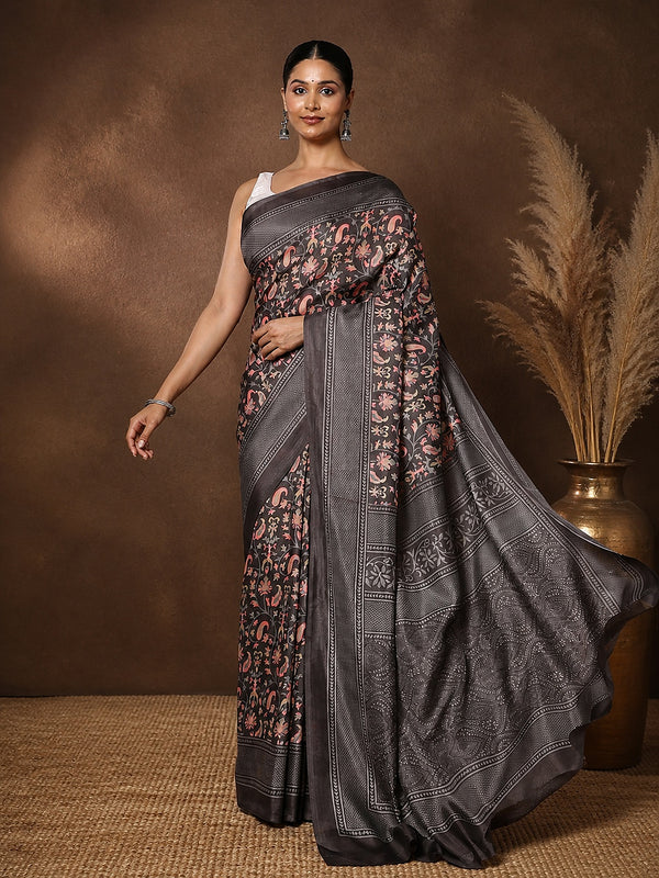 Charcoal grey printed saree with a floral and paisley print in pink, mustard and green, framed by a wide decorative border.