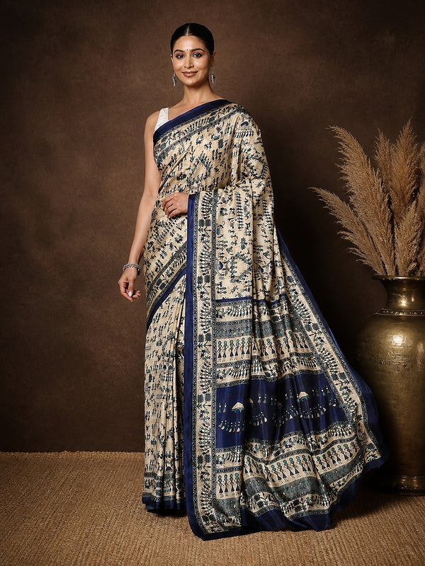 Beige printed Kashmiri silk saree with an all-over Warli-style figurative print of navy tribal figures, huts and trees, a wide navy pallu panel and a geometric navy border.