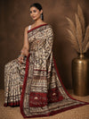 Beige printed Kashmiri silk saree with a two-tone maroon Warli-style figurative print of tribal figures and trees, and a wide maroon border stacked with rows of figures.