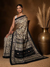 Beige printed Kashmiri silk saree with a graphic black Warli-style figurative print of tribal figures, huts and trees, a wide black pallu of figure bands, and a narrow black border.